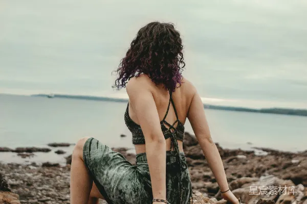 高清摄影 一个女人坐在岩石上，旁边是大海。