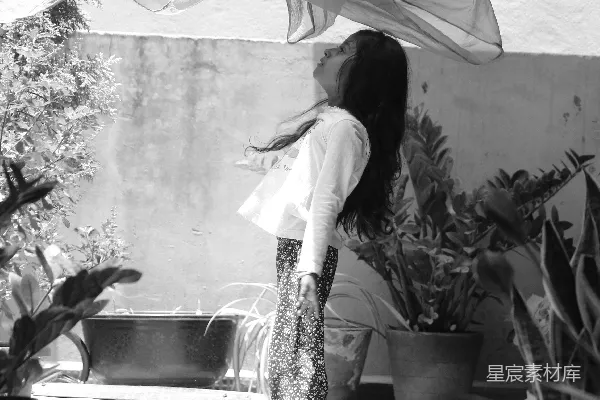 高清摄影 白色上衣、长袖、黑色与白色条纹 skirt 的女人站在绿色植物旁边