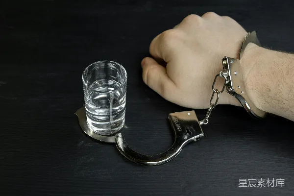 高清摄影 一个男人的手戴着手铐，手里拿着一杯水