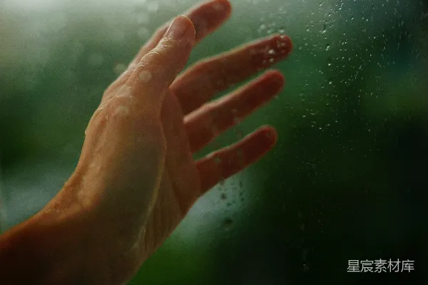 高清摄影 一只手触摸着带有绿色背景的雨窗玻璃。