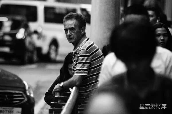 高清摄影 男士靠在栏杆附近，旁边有行人行走。