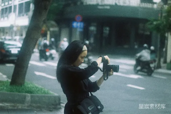 高清摄影 一位女性在城市街道上拍摄一座建筑的照片。