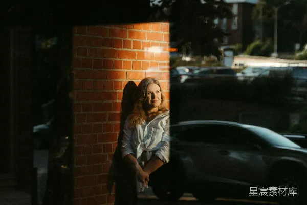 高清摄影 一个女人倚靠在一条砖墙旁的 sidewalk 上