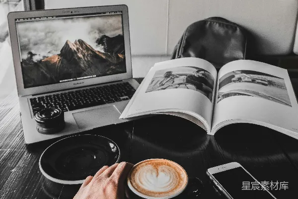 高清摄影 男士手持一杯拿铁咖啡，桌上摆放着一台MacBook Air和一本书。