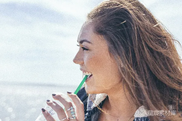 高清摄影 女人穿着黑色和灰色的夹克，拿着玻璃杯在白天靠近水体处喝饮料。