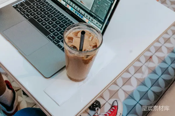 高清摄影 macbook pro旁边放着一个透明塑料杯，里面装着棕色的液体。