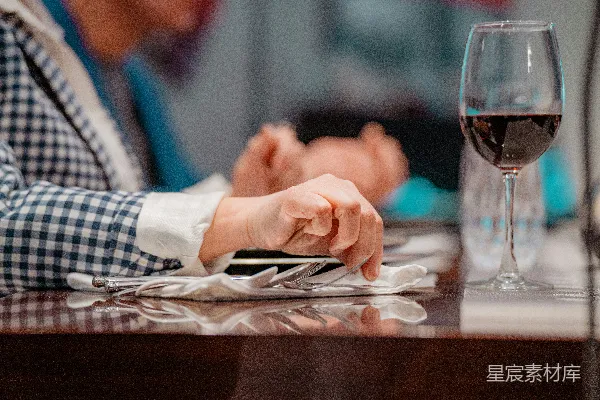 一个坐在桌子旁的人手中拿着一杯葡萄酒。