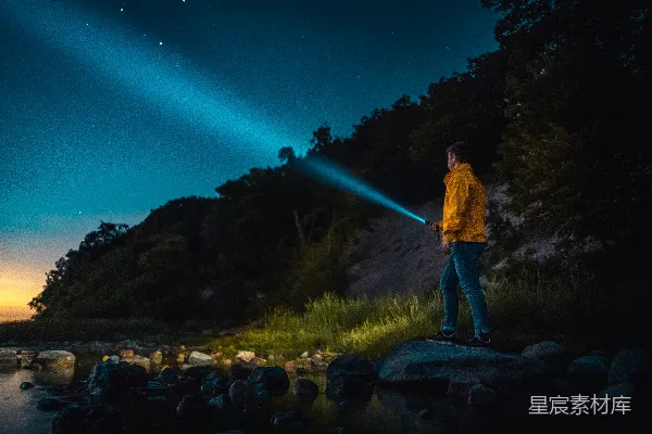 男人手持手电筒站在灰色石头上，夜间的场景