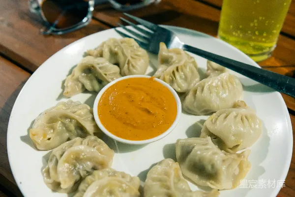 高清摄影 一个白色盘子上放着饺子，旁边是一杯酱料。