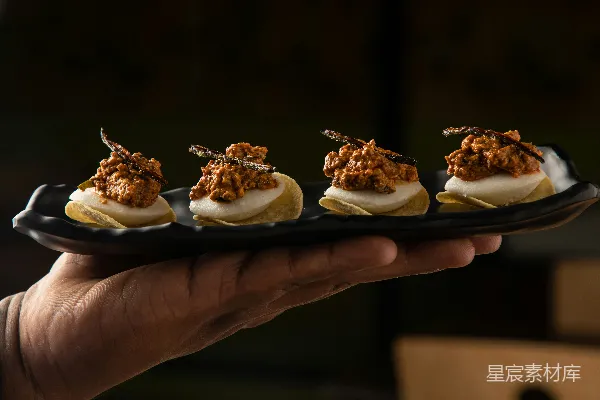 高清摄影 一只手拿着一个上面摆放着小 appetizer 的黑色盘子