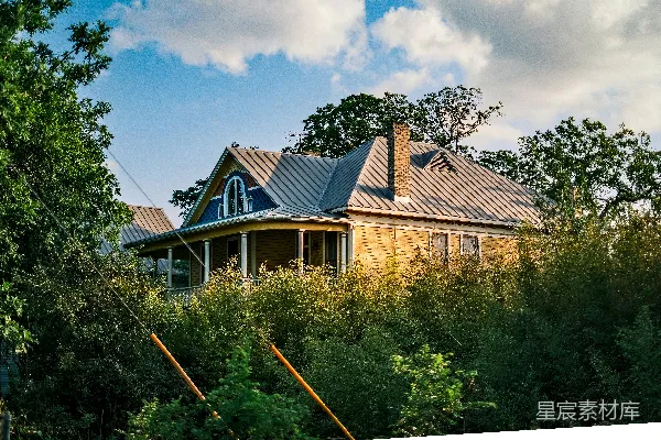 高清摄影 乡村风格的小屋，蓝色屋顶和门廊旁绿树环绕。