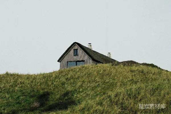 高清摄影 一座小屋坐落在草地上的一座小山上。