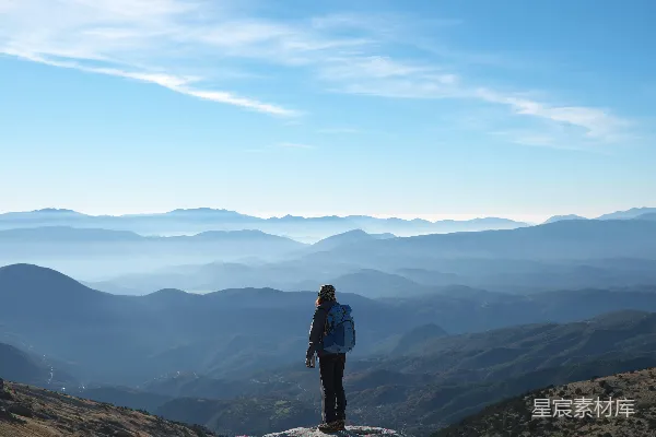 高清摄影 背着背包站在山崖上，面向群山的白天场景
