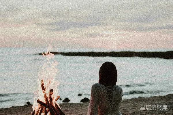高清摄影 一个女人坐在海滩前的篝火旁。