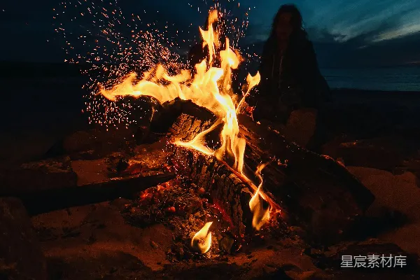 高清摄影 穿着黑色夹克的男人站在篝火旁边，夜幕降临时分。