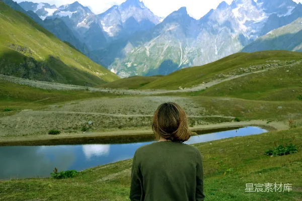绿上衣的女人站在湖边山间的绿色草地上，白天场景