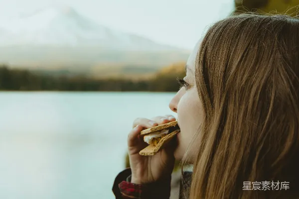 高清摄影 站在水边，面对着山景，吃东西的女人