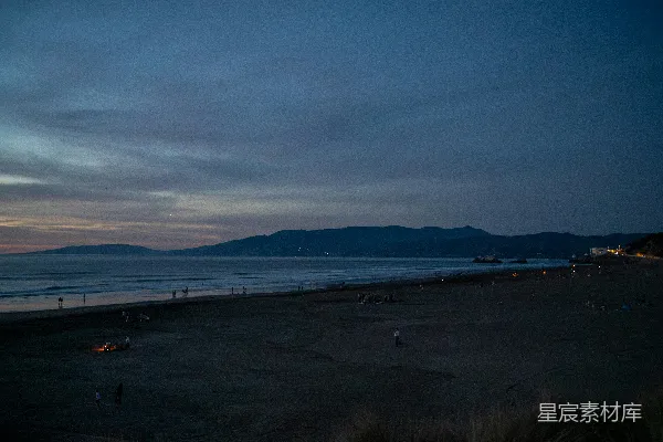 高清摄影 夕阳笼罩着一片广阔的海滩，远处是海洋和连绵的山脉。