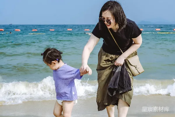 高清摄影 一位母亲和一个孩子手牵手在沙滩上散步。