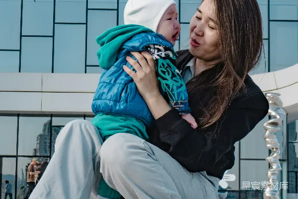 高清摄影 一位母亲抱着一个婴儿站在现代化的建筑前。