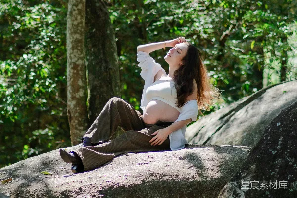 高清摄影 怀孕的女性坐在森林中的大岩石上
