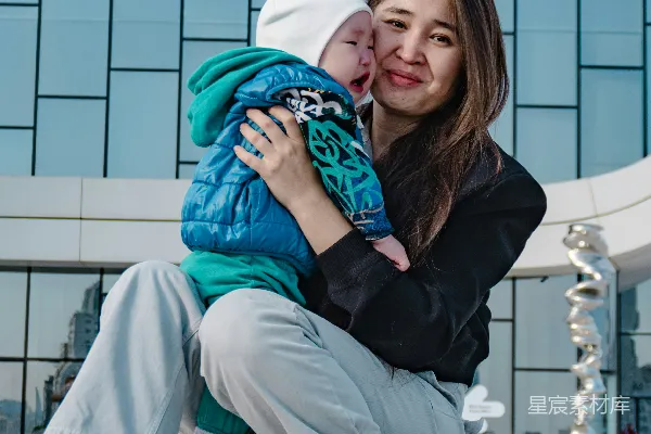 高清摄影 一位母亲抱着她的婴儿，背景是一座现代化的建筑。