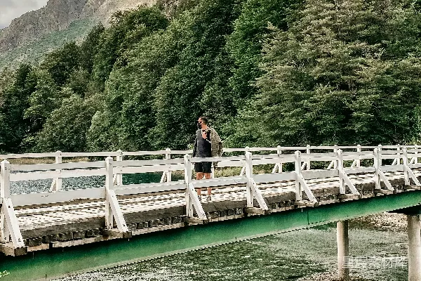 几人在河边的一座桥上，背景是树木和山峦。