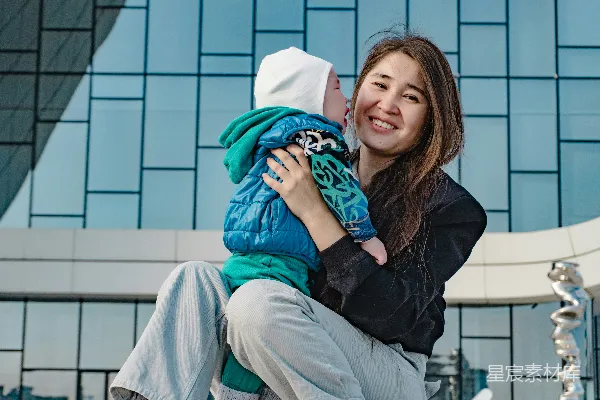 高清摄影 母亲抱着她的婴儿站在一座现代化建筑前。