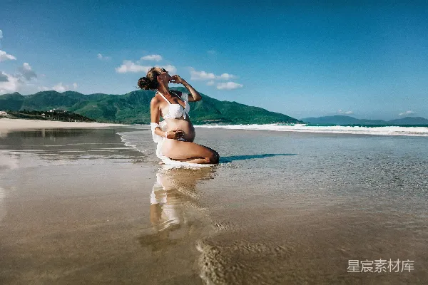 高清摄影 怀胎的女人站在潮湿的沙滩上摆姿势。