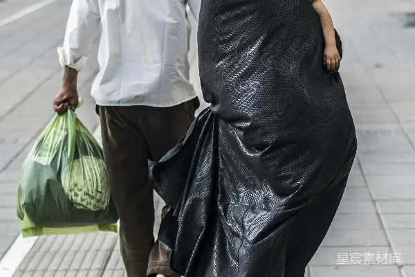 高清摄影 穿着黑色连衣裙的女人拿着一个绿色塑料袋。