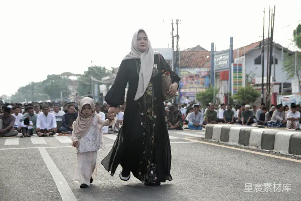 高清摄影 一对妇女和孩子在街上行走，旁边有人在祈祷。