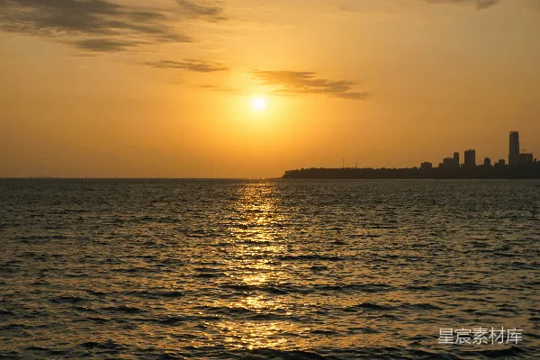 高清摄影 夕阳落下海面上，远处有一座城市。