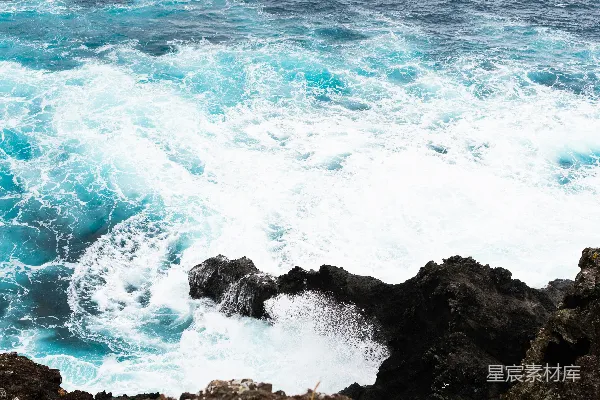 白天海浪撞击黑色岩石形成的悬崖景观