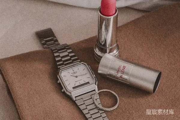 高清摄影 床上有一只手表、一支口红和另一只手表。