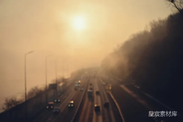 雾蒙蒙的高速公路上汽车在日出时分行驶。