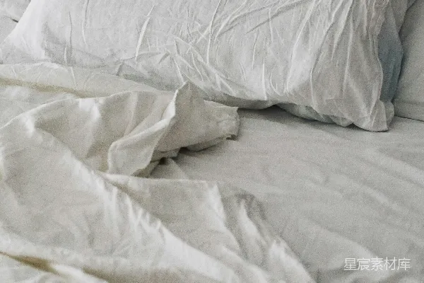 高清摄影 一张床上铺着皱巴巴的白色被子和枕头。