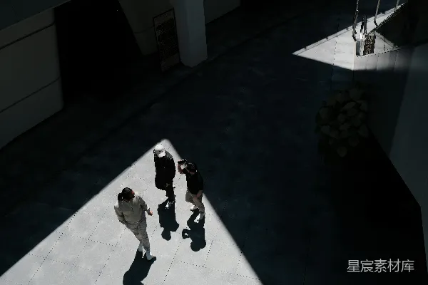 高清摄影 三个人在一个阳光明媚、阴影笼罩的现代化建筑中行走。
