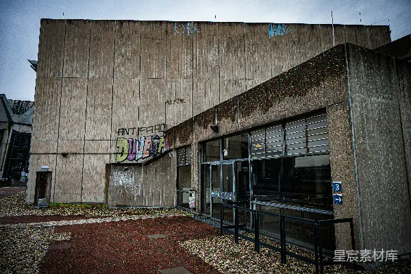 粗野主义混凝土建筑，外有涂鸦和玻璃入口。