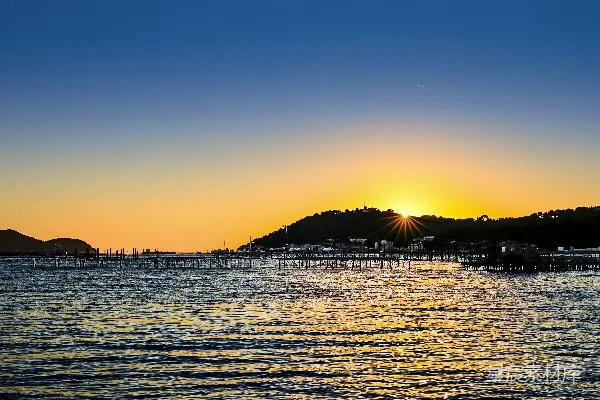 夕阳映照平静的海洋，远处有起伏的山峦。