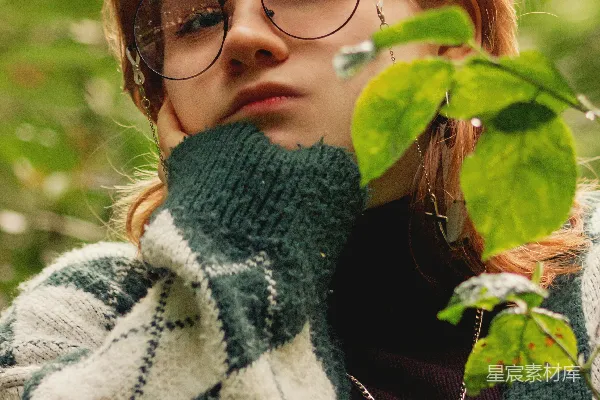 戴眼镜的女士正在拿着一片绿叶。