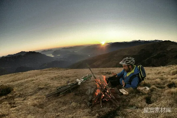 男人躺在棕色的草地上，在日出前的篝火旁打盹。