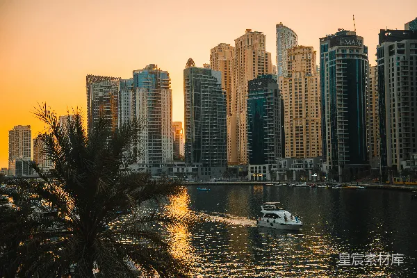 一艘船在夕阳下漂浮于水面，城市中的高楼大厦矗立其旁。