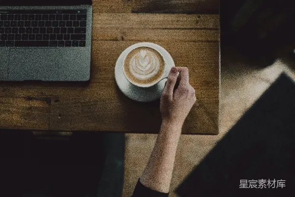 桌子上的人拿着一杯咖啡，旁边是笔记本电脑。
