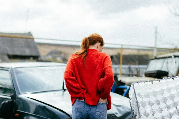 一个穿着红色毛衣的女人站在一辆汽车旁边。
