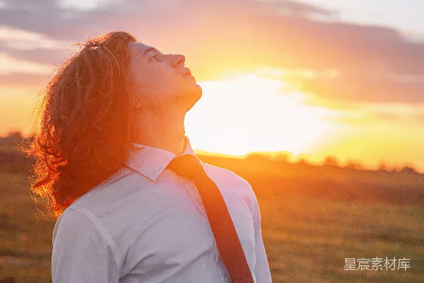 一个男人站在一片空地上，太阳正在他的背后落下。