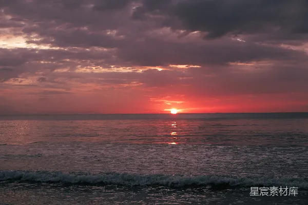 在一片云层覆盖的晴天里，夕阳正沉入大海。