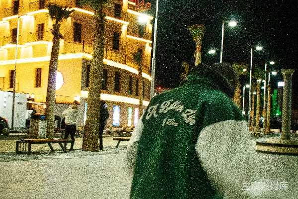 高清摄影 穿绿色夹克的人在夜晚的城市街道上行走。