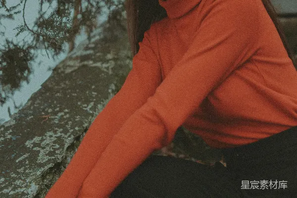 一个穿红色上衣的女人正坐在一块岩石上。