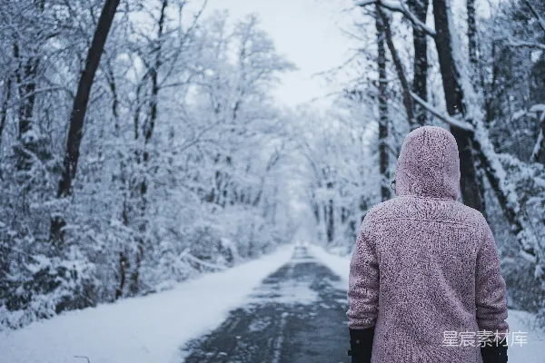 一个穿着粉红色夹克的人正在一条被白雪覆盖的路面上行走。