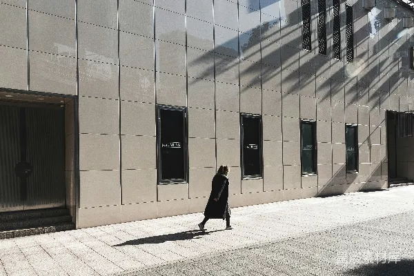 高清摄影 穿着黑色长袖连衣裙的女子正沿着建筑物旁行走。